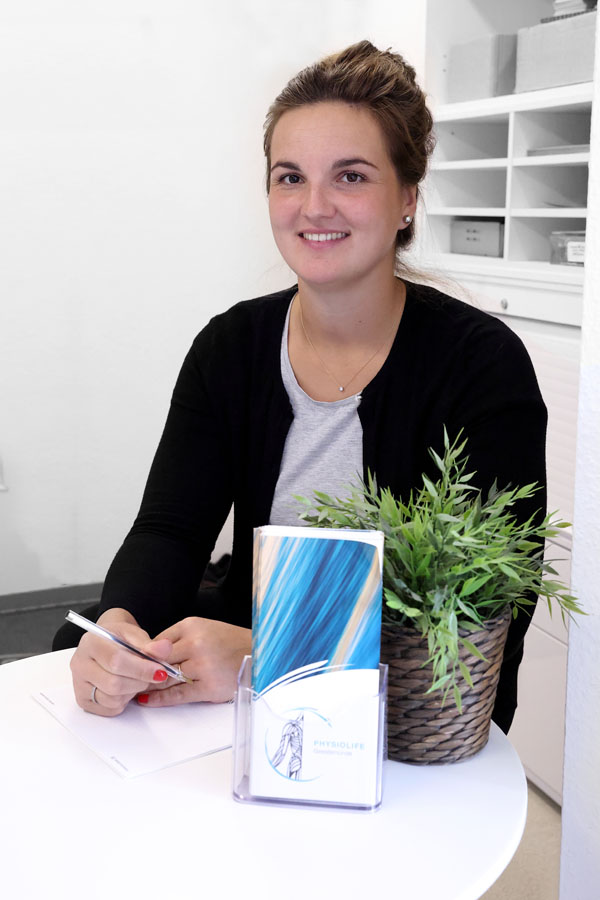 Eine junge Frau sitzt an einem Tisch und guckt in die Kamera.